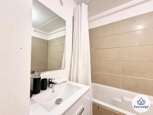 La salle de bains est pourvue d'un lavabo, d'une baignoire et d'un miroir. dans l'établissement Kheyl Home 2 étoiles - T3 de 47 m2 à Saint-Denis, à Saint-Denis