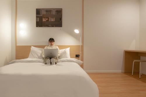 a person sitting on a bed using a laptop at Aank Hotel Cheonan Station 1st in Cheonan