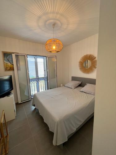 um quarto com uma cama branca e um lustre em Appart avec terrasse vue sur mer exceptionnelle em L'Île-Rousse