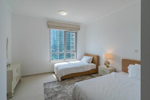 a white bedroom with two beds and a window at Splendid Apartments with Burj Khalifa and Fountain View in Dubai