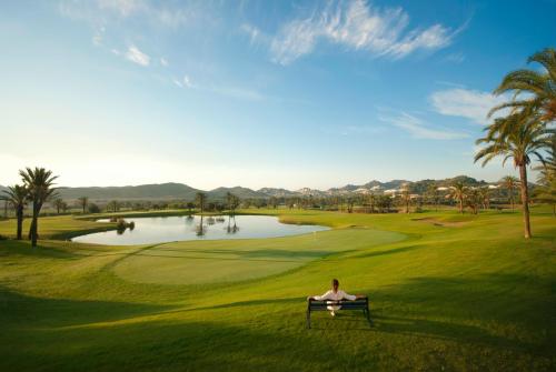 a woman sitting on a bench in front of a golf course at Grand Hyatt La Manga Club Golf & Spa in La Manga del Mar Menor