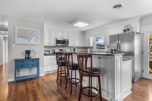 una cocina con armarios blancos y un bar con taburetes en Otter Banks Retreat home, en Harkers Island