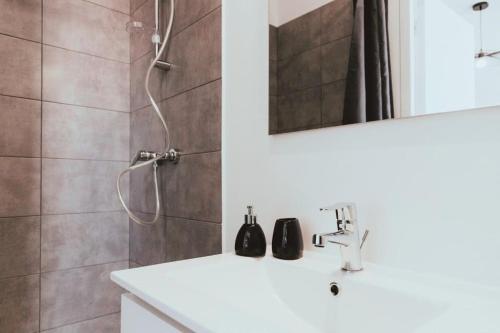 La salle de bains est pourvue d'un lavabo blanc et d'une douche. dans l'établissement NEPTUNE - Appartement Moderne & élégant, à Saint-Étienne