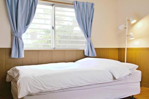 Bett in einem Schlafzimmer mit einem Fenster mit blauen Vorhängen in der Unterkunft ピースリー安里201 in Tomari