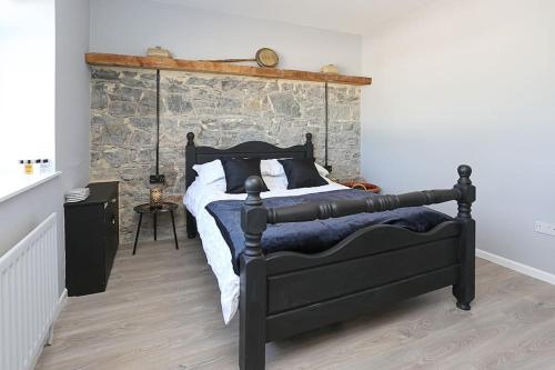a bedroom with a black bed with a stone wall at Briglane Cottage in Kirkistown