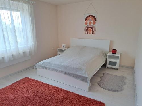 a white bedroom with a bed and a red rug at Corner Vendégház - Zánka in Zánka
