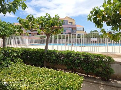 une clôture avec un arbre devant un bâtiment dans l'établissement Les Barcarelles résidence entre montagne et mer, au Barcarès