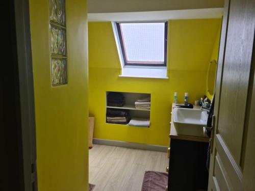 une salle de bains jaune avec lavabo et fenêtre. dans l'établissement The Cat ,maison de vacances à 50m de la plage, à Le Portel