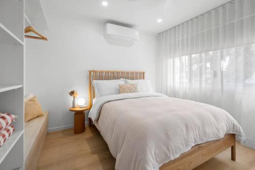 a white bedroom with a bed and a window at Vibes At Five Noosa in Noosaville