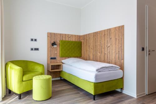 ein Schlafzimmer mit einem Bett und einem grünen Stuhl in der Unterkunft Hotel Fuchsbau Jüterbog in Jüterbog