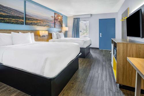 a hotel room with two beds and a flat screen tv at Days Inn by Wyndham Raleigh Glenwood-Crabtree in Raleigh