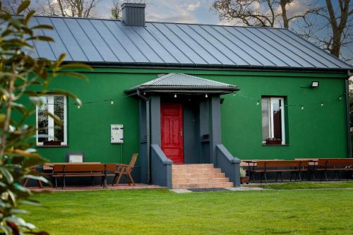 a green house with a red door and benches at Ranczo u Loni 