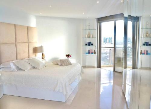 a white bedroom with a white bed and a glass door at Daniel Hotel - Residence Seaside Luxury Flat in Herzliya