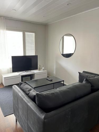 ein Wohnzimmer mit einem schwarzen Sofa und einem Flachbild-TV in der Unterkunft Rauhallinen paritalo, Sauna, Terassi, Grilli in Lehmonaho
