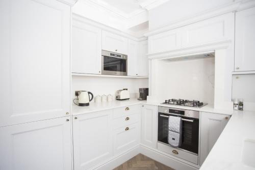 Biała kuchnia z białymi szafkami i urządzeniami w obiekcie Coachman's Cottage- Worthing Beach sleeps 9 w mieście Worthing