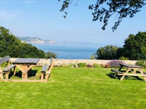 two picnic tables and benches in a field with the ocean at Sea Cliff View Designer Home in Lyme Regis