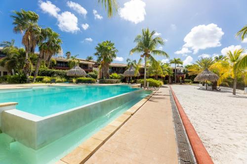 a resort swimming pool with palm trees and a beach at Spanish Water Apartments in Willemstad