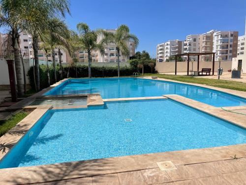 a large blue swimming pool with palm trees and buildings at Chic & cosy Flat Near Airport lockbox fast wifi in Nouaceur