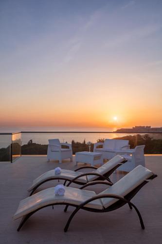 a sunset over the ocean with white chairs and tables at Acapulco Resort Hotel in Kérynia