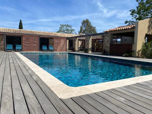 una piscina con terraza de madera junto a una casa en Magnifique villa avec piscine au coeur des vignes en Cogolin