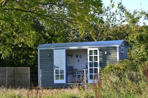 a small shed with a white door in a field at The Nutbourne Hut - shepherd's hut - pint-sized luxury in Hambrook