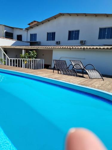 a swimming pool with two chairs and a building at Pousada Coqueiral in Aracruz