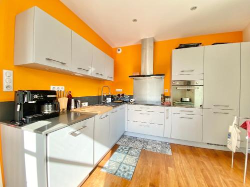 - une cuisine avec des placards blancs et un mur orange dans l'établissement LE QUAI 18 - Luxe - Plein Centre - Vue dur les quais - Wifi - Parking, à Quimper