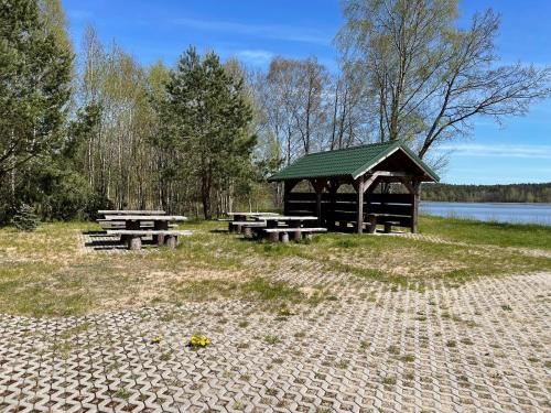 a gazebo and picnic tables in front of a lake at Żurawia Łąka in Bytów
