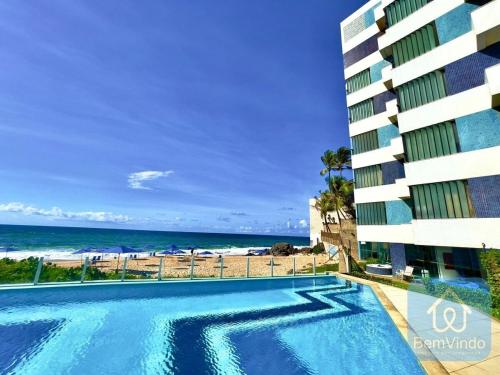uma piscina em frente a um edifício e à praia em Apartamento completo e pé na areia no Rio Vermelho em Salvador