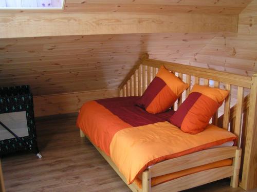 a wooden bed with two orange pillows in a room at Les Chalets du Choumeau in Saint-Léger-les-Mélèzes