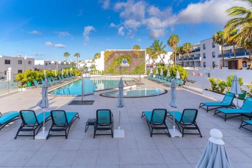 a patio with chairs and a pool with palm trees at Rosamar Apartamentos in Puerto del Carmen
