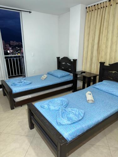 Habitación con 2 camas con sábanas azules y balcón. en Hospedaje Balcones de la Colina, en Floridablanca