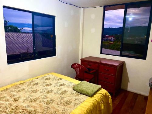 ein Schlafzimmer mit einem Bett, einer Kommode und zwei Fenstern in der Unterkunft Casa nómada Puyo in Puyo