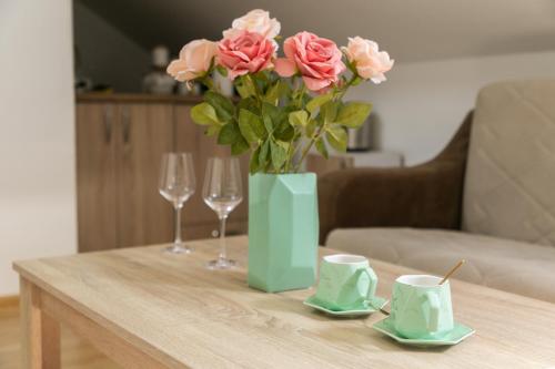 a table with a vase of pink roses and two glasses at APARTMAN MIKI BIJELO POLJE in Bijelo Polje
