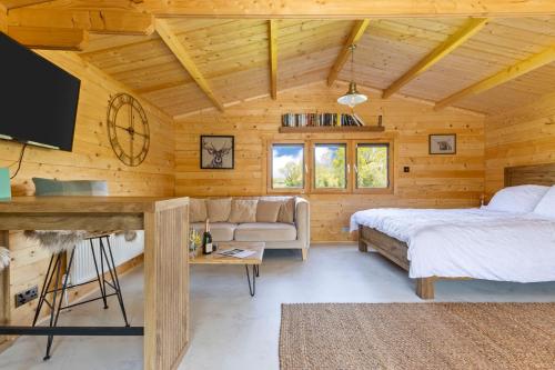Dormitorio en cabaña de madera con cama y sofá en Choller Lake Lodges - Sunbeam Cabin With Private Hot Tub en Arundel