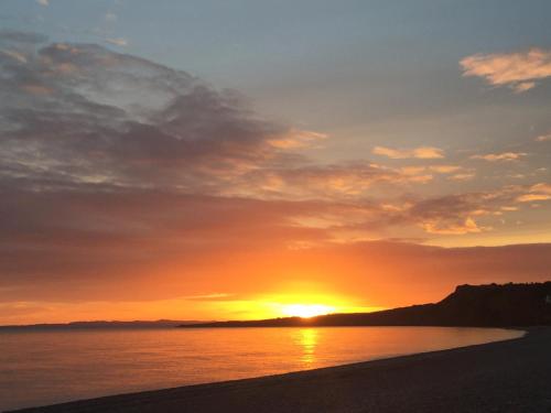 a sunset on a beach with the sun setting at Bowhayes Farm - Camping & Glamping - Bell Tents - Cider Orchard in Venn Ottery