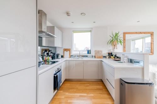 a white kitchen with white cabinets and a wooden floor at Modern Bermondsey Apartment in London