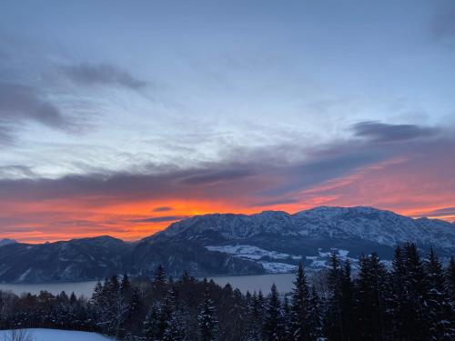a sunset over a mountain range with trees and a lake at moderne Apartments am Attersee Dachsteinblick - ruhige Lage mit traumhaften Blick in Nussdorf am Attersee