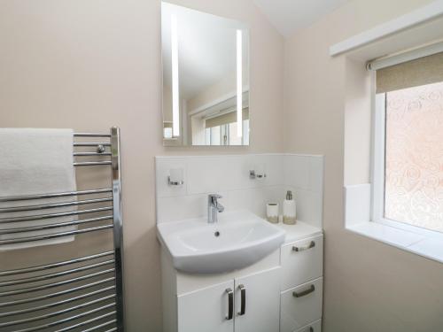 W białej łazience znajduje się umywalka i lustro. w obiekcie Kennedy's Cottage w mieście Ashbourne