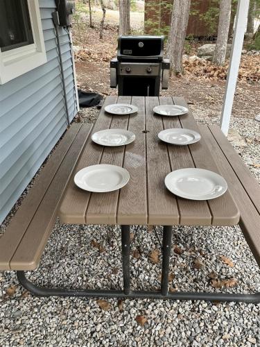 a wooden picnic table with plates on it next to a grill at ANY SEASON ESCAPE LIMIT 10 villa in Bridgton