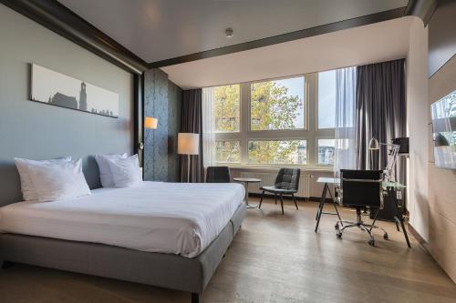 Habitación de hotel con cama, escritorio y ventanas en Leonardo Hotel Utrecht City Center en Utrecht