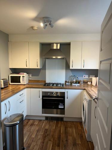 La cuisine est équipée de placards blancs et d'un four avec plaques de cuisson. dans l'établissement Newbuild - 3 bedrooms, 2 baths,5 mins from airport, à Édimbourg