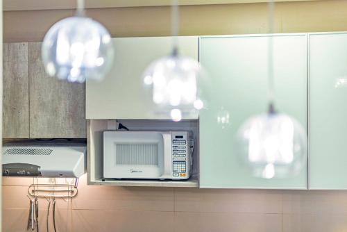 a kitchen with white cabinets and a microwave and chandeliers at Vista do Vale! 400 metros da Rua Coberta - Acomoda até 4 hóspedes in Gramado