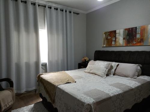 a bedroom with a bed with white curtains and a window at Casa da Nice in Guaratinguetá