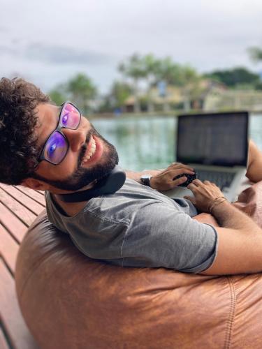 a man with glasses laying on a chair with a laptop at Nômades Riverside - Adventure Hostels & Coworking in Florianópolis