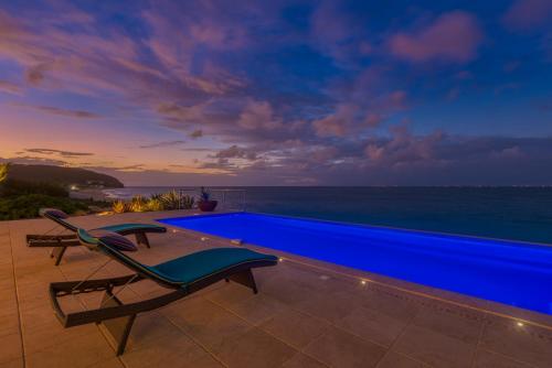 a blue swimming pool with a chair and the ocean at Villa La Vie en Bleu in Marigot