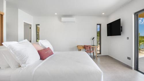 a bedroom with a white bed with pillows and a tv at Villa Enjoy in Les Terres Basses