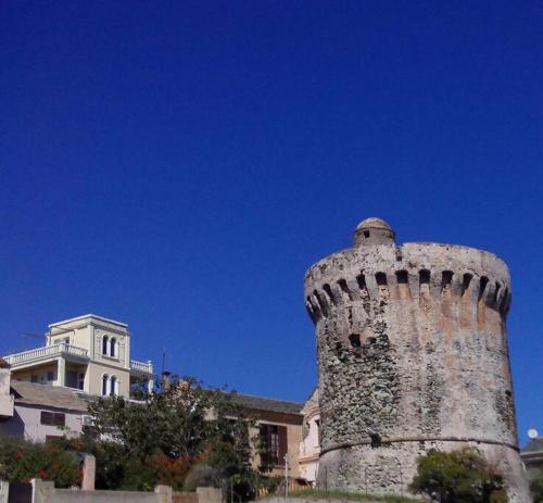 un bâtiment avec une tour devant un bâtiment dans l'établissement Appartement de charme, T3, situation idéale, pieds dans l'eau, Cap Corse, à La Vasina