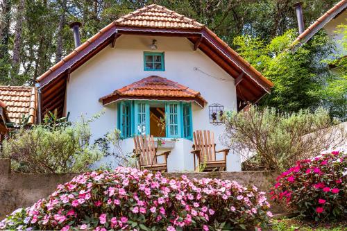 a small white house with blue windows and flowers at Pousada Vila Suiça in Monte Verde