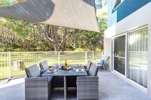 a patio with a table and chairs on a balcony at Banksia at Fingal 1 92 Rocky Point Rd Aircon spa and Wi Fi in Fingal Bay